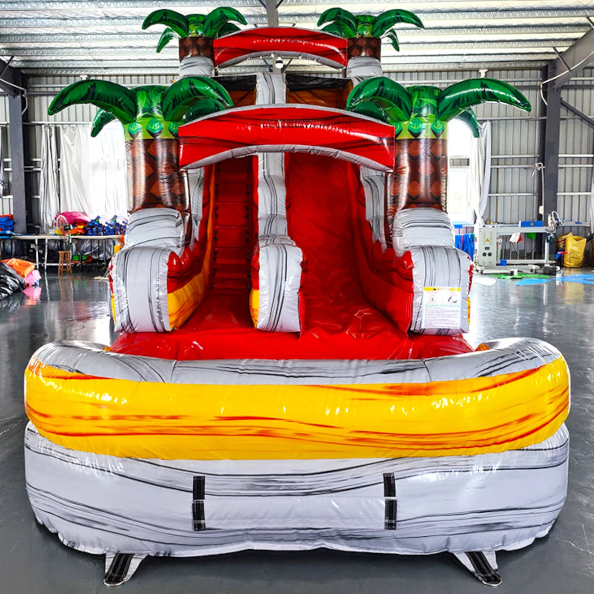15ft Fire Island Commercial Single Lane Inflatable Water Slide front view showcasing red slide, inflatable palm trees, and yellow splash pool in warehouse setting