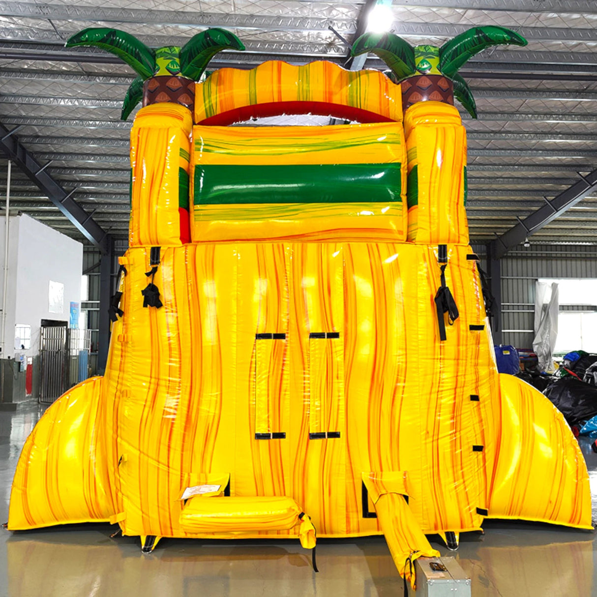 15ft Rasta Splash Commercial Single Lane Inflatable Water Slide featuring tropical-themed design with palm trees, yellow structure, red slide, and inflatable pool area in warehouse setting