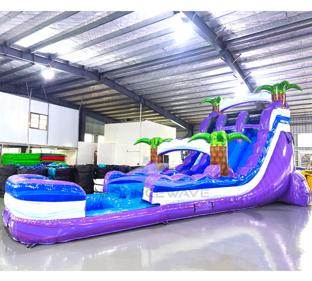 Side view of Purple Thunder hybrid water slide in indoor facility, showcasing its length, dual purple sliding lanes, palm tree decorations, and extended blue splash pool area.