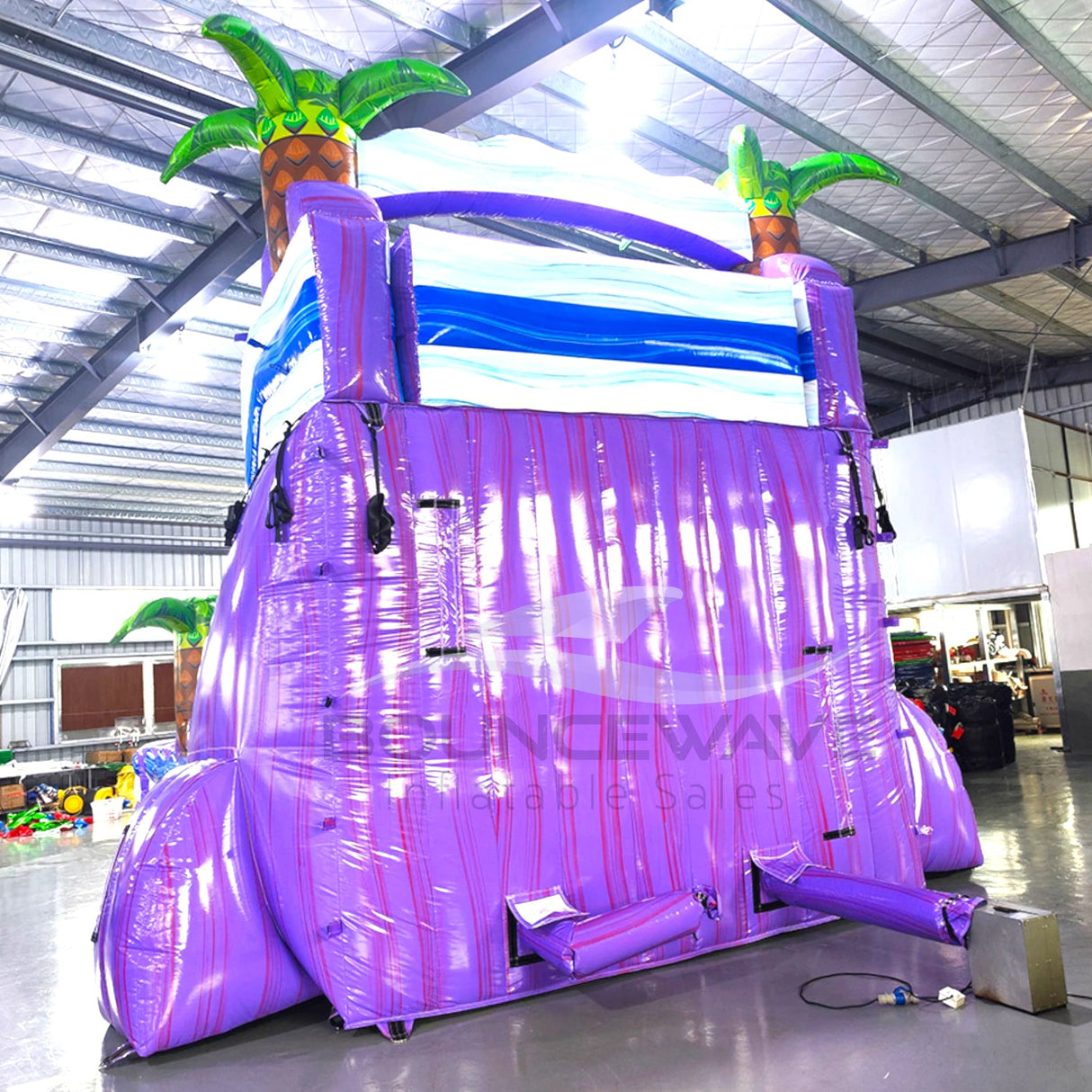 Rear view of Purple Thunder inflatable water slide, displaying tall purple structure with climbing area, safety features, and tropical-themed top section with palm trees