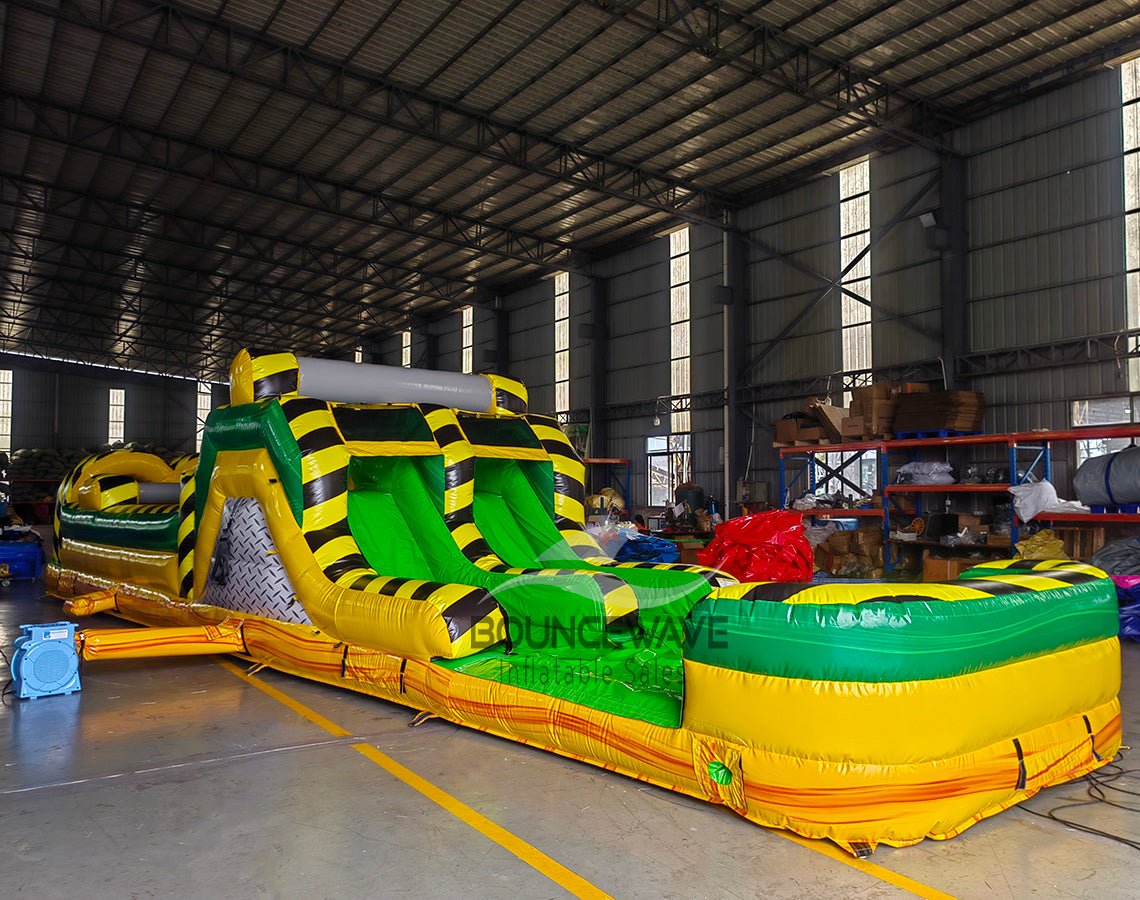 46ft Toxic Open Air Hybrid Inflatable Obstacle Course side view showcasing long yellow structure with black caution stripes, various obstacles, and green flooring in indoor facility