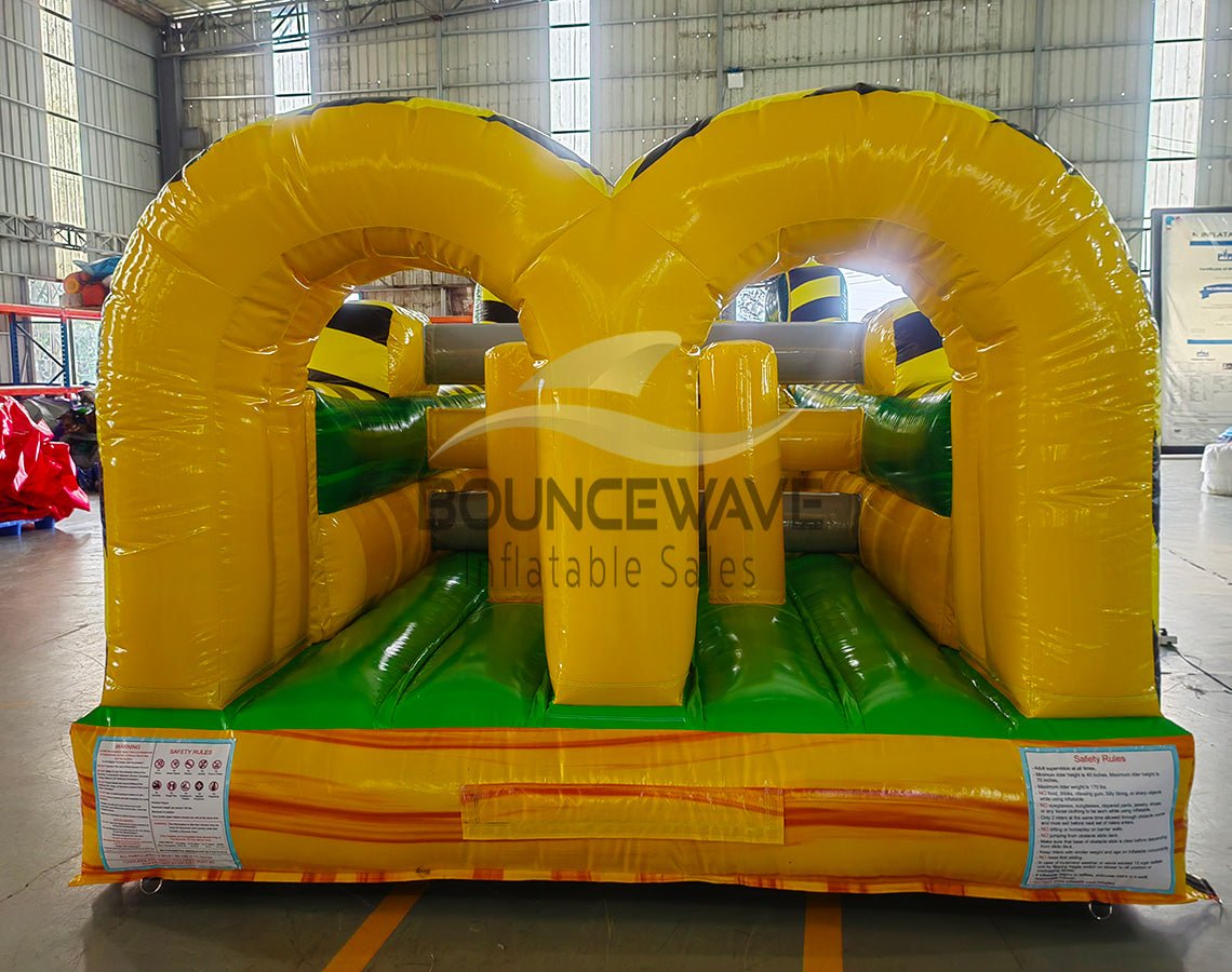 46ft Toxic Open Air Hybrid Inflatable Obstacle Course front view highlighting yellow and black caution-themed design, arched entrances, and green floor in indoor facility