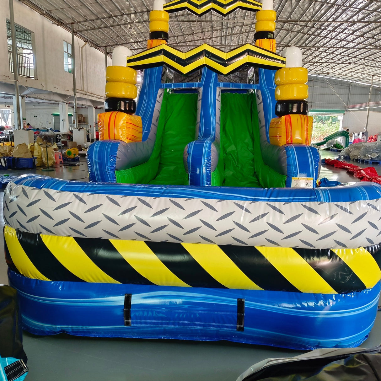92ft Radioactive Run 3-Piece Wet/Dry Inflatable Obstacle Course side view displaying yellow and black caution-striped design, green slides, and blue inflatable base in indoor facility
