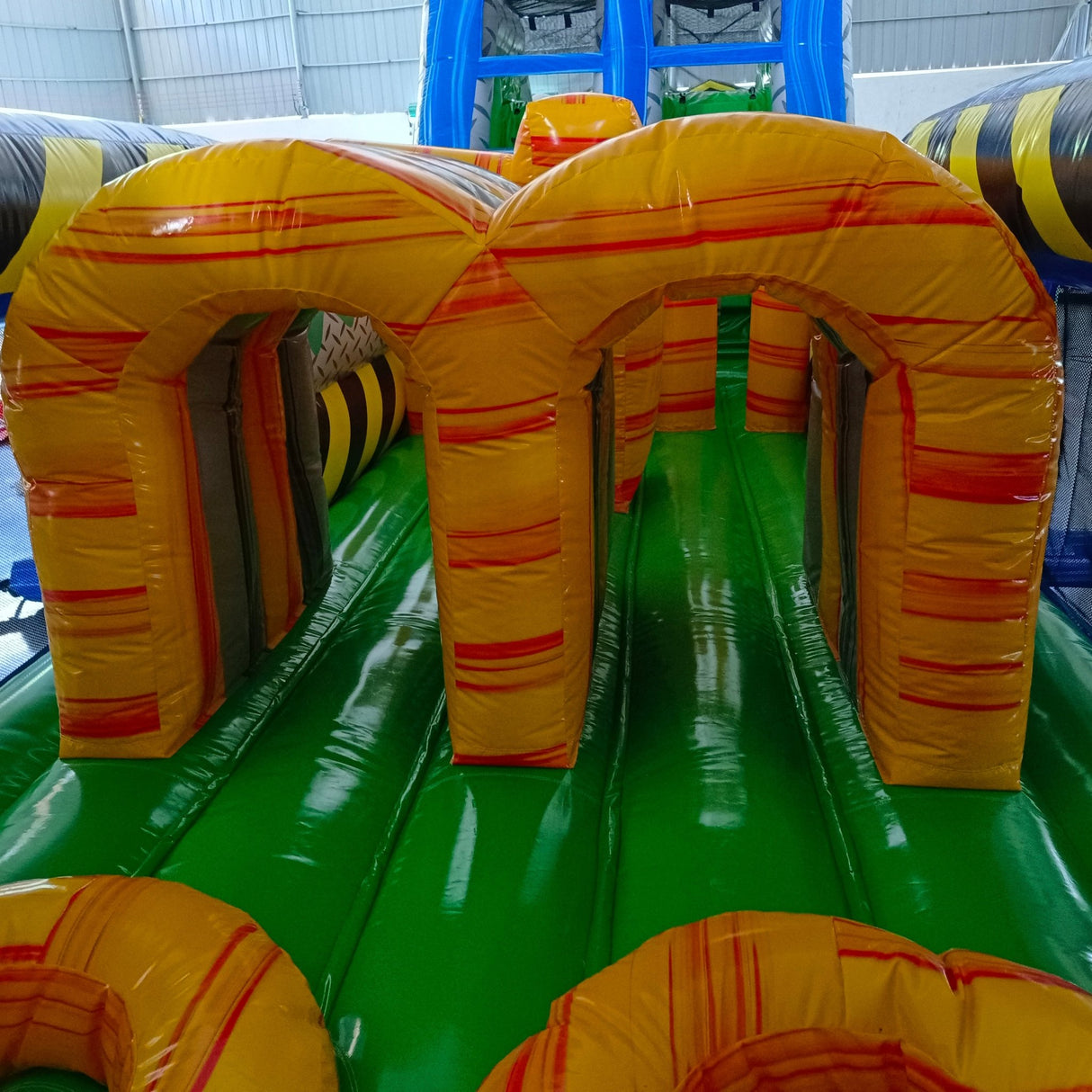 92ft Radioactive Run 3-Piece Wet/Dry Inflatable Obstacle Course close-up of yellow inflatable arches with red stripes on green base, part of larger obstacle course