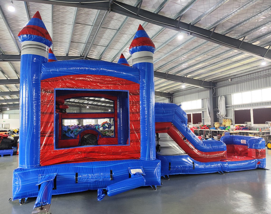 Castle-themed inflatable combo with bounce house, slide, and splash pool. Decorated with blue walls, red turrets, and mesh windows. Displayed in an indoor facility with various other inflatable products and equipment visible.