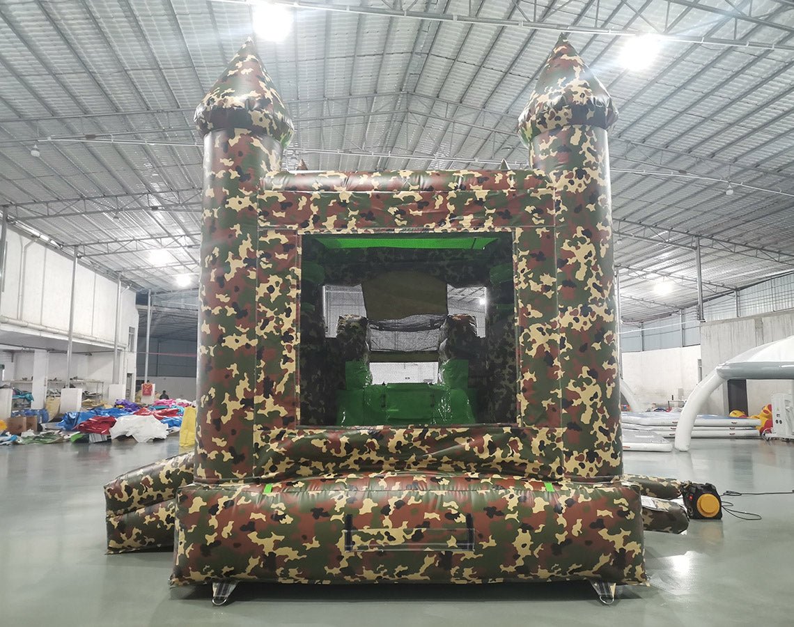 Front view of Camo Econo Combo, showcasing the bounce house entrance with camouflage design, mesh windows, and two pointed turrets. The combo includes a slide and splash pool area. Displayed in an indoor facility with other inflatable products visible.
