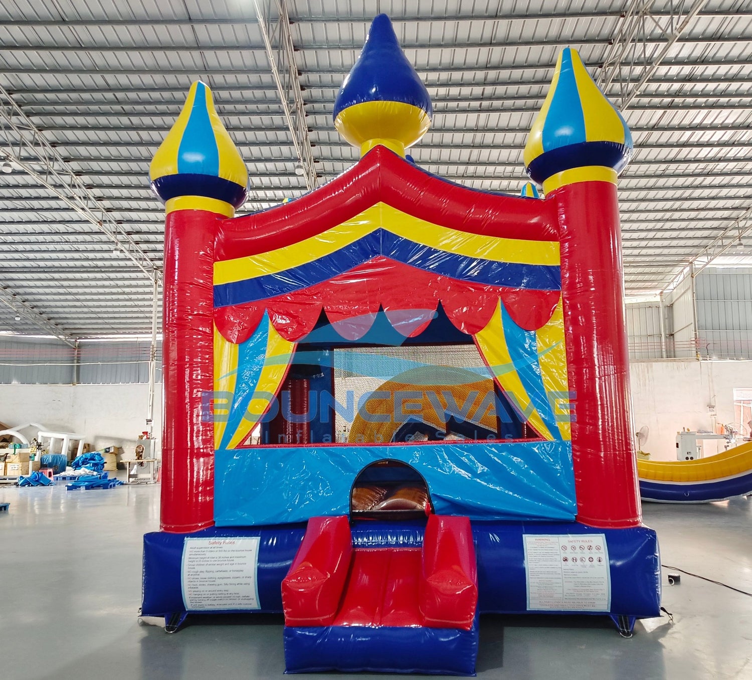 Carnival Commercial Grade Bounce House in warehouse setting, showcasing colorful castle design with mesh windows and inflatable columns