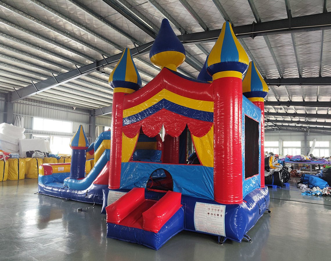 Front view of Carnival Econo Combo, showcasing the bounce house entrance with red pillars, blue and yellow spires, and a colorful awning. The combo includes a slide and splash pool area. Displayed in an indoor facility with metal roofing and other equipment visible.