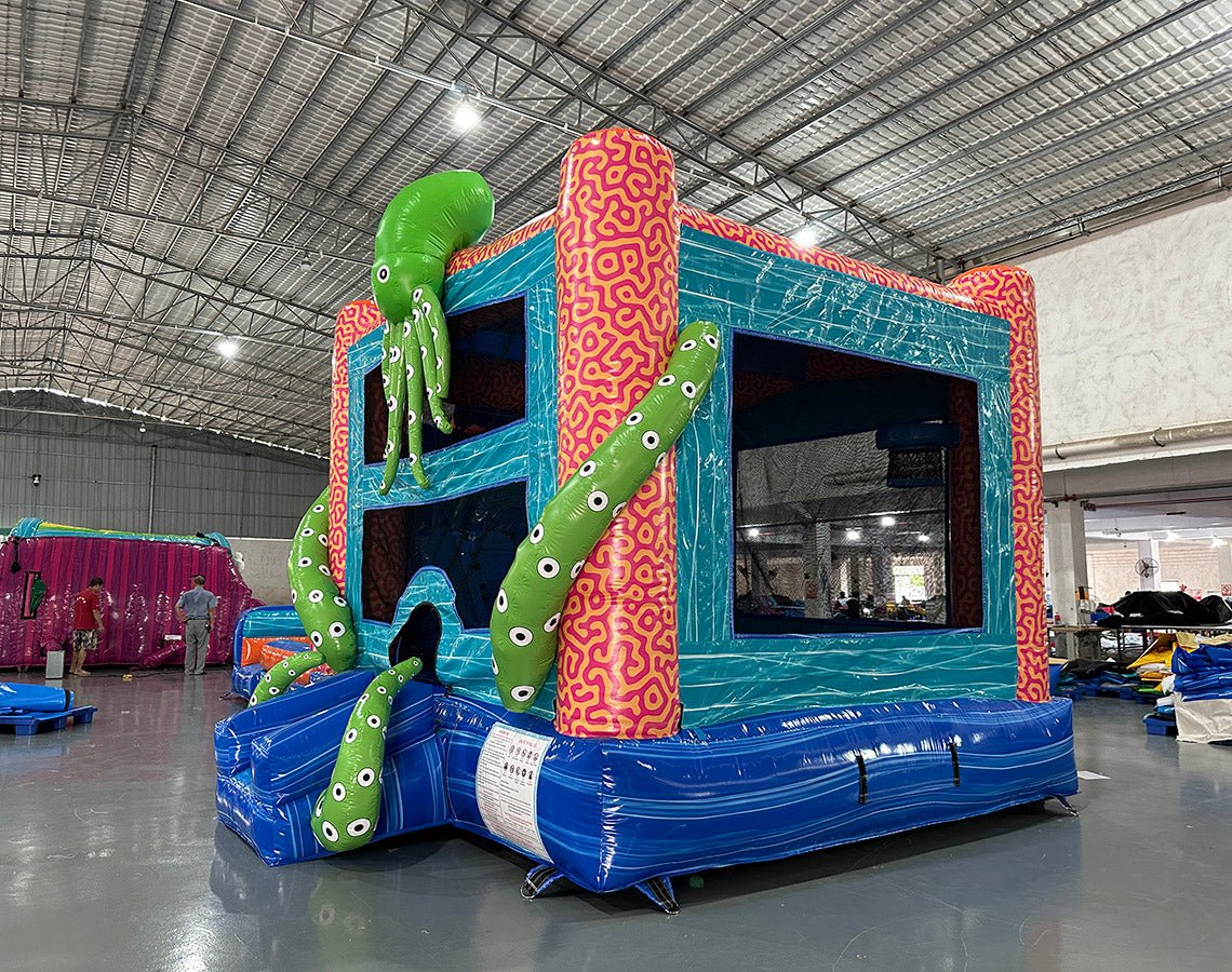 Close-up view of the bounce house entrance of Deep Sea Dive Dual Lane Commercial Inflatable Combo. Shows the blue wave-patterned base, green tentacles with eyes, and part of the orange octopus. The bounce house area is visible with mesh windows and a coral-patterned interior. Set in a warehouse with concrete flooring and other inflatable products in the background, showcasing its commercial use.
