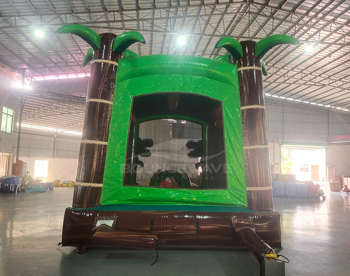 Dino Dive Commercial Grade Bounce House with tropical theme, palm trees, and inflatable dinosaurs in warehouse setting