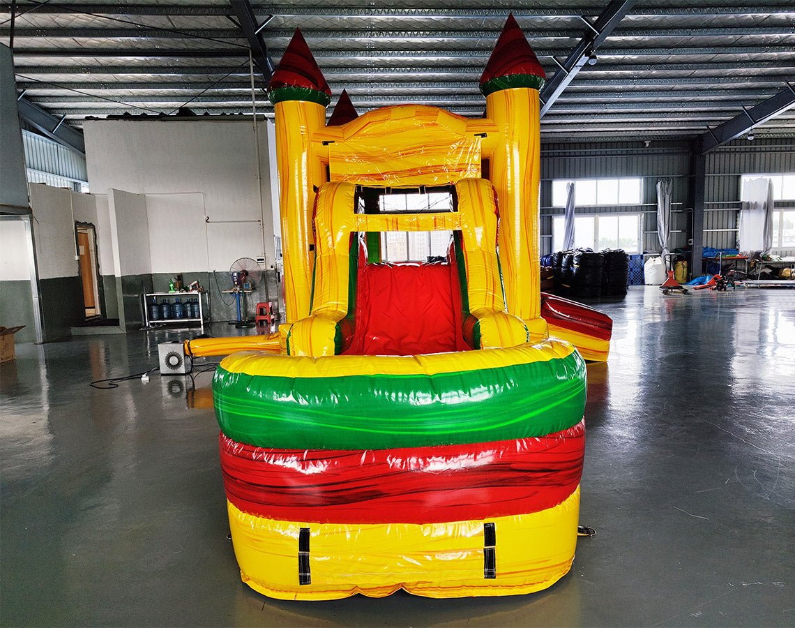 Close-up front view of Rasta Splash Commercial Econo Inflatable Combo (Wet/Dry) highlighting the entrance with yellow base, red turrets, and green accents. The inflatable features a red interior visible through the mesh entrance. Set up on a polished concrete floor in an indoor warehouse, showcasing its vibrant rasta-inspired color scheme.