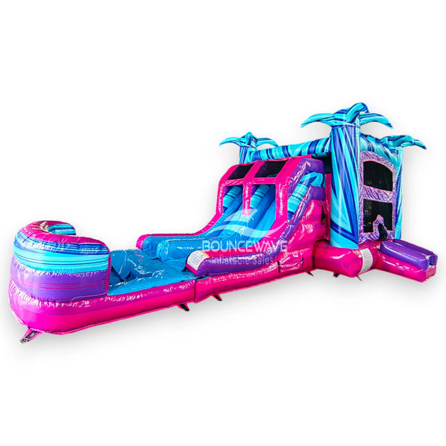 Supernova Dual Lane Commercial Inflatable Combo (Wet/Dry) featuring vibrant blue and pink design with palm tree decorations, dual slides, and extended splash pool in warehouse setting