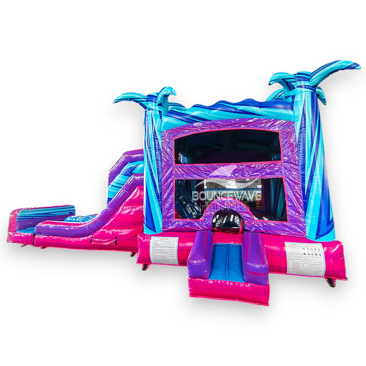 Supernova Dual Lane Commercial Inflatable Combo (Wet/Dry) front view highlighting blue inflatable palm trees, pink and purple slides, bounce house entrance, and safety instructions