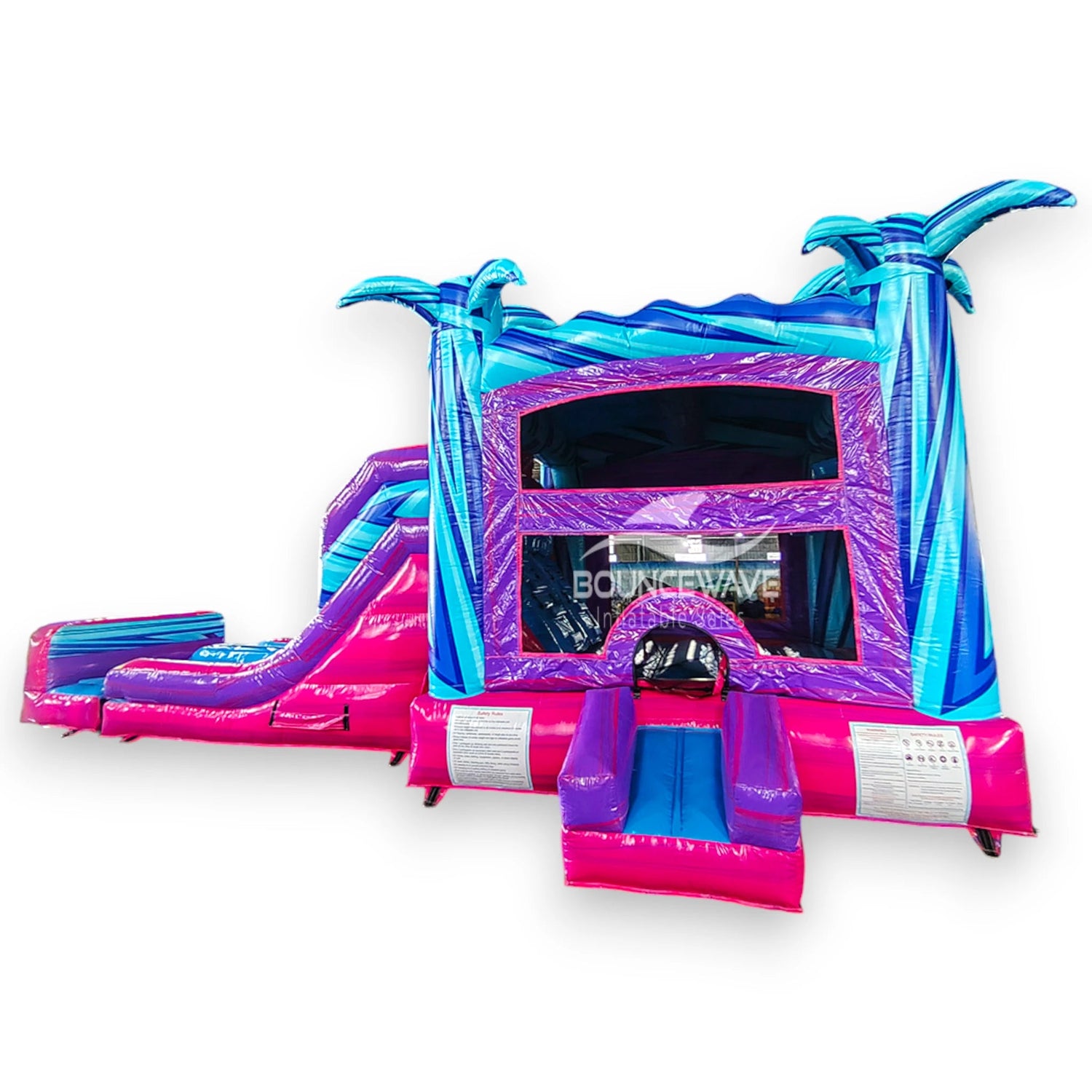 Supernova Dual Lane Commercial Inflatable Combo (Wet/Dry) front view highlighting blue inflatable palm trees, pink and purple slides, bounce house entrance, and safety instructions
