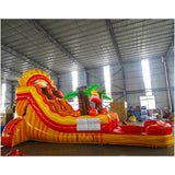  Inflatable tropical-themed water slide with yellow and red curves, palm tree decorations, and a single lane, set up in a large indoor warehouse