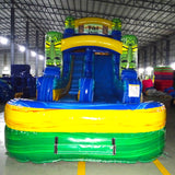 Front view of Tiki Shot single lane water slide in indoor warehouse, showing tall structure with blue sliding surface, tiki mask designs, and large splash area with yellow and green colors.