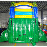 Rear view of Tiki Shot inflatable water slide, displaying tall green structure with climbing area, safety features, and tropical-themed top section with tiki masks and yellow accents.