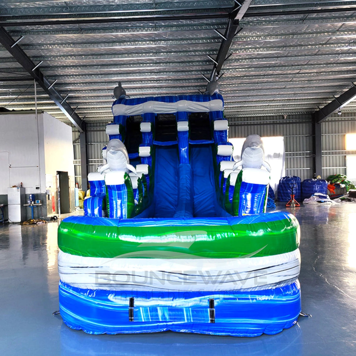 Front view of dolphin-themed inflatable water slide in indoor setting, showing dual lanes and large splash pool.
