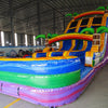 Side view of the 18ft Goombay Splash Center Climb water slide, showcasing its three blue sliding lanes, yellow borders, inflatable palm trees, rainbow arch, and large multicolored splash pool area, set up in a spacious indoor warehouse.