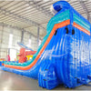 Large inflatable water slide with ocean theme, featuring blue sliding lanes, shark decorations, and a spacious splash pool area with octopus tentacles. The slide combines open and enclosed sections, set up in an indoor warehouse with metal roofing visible.