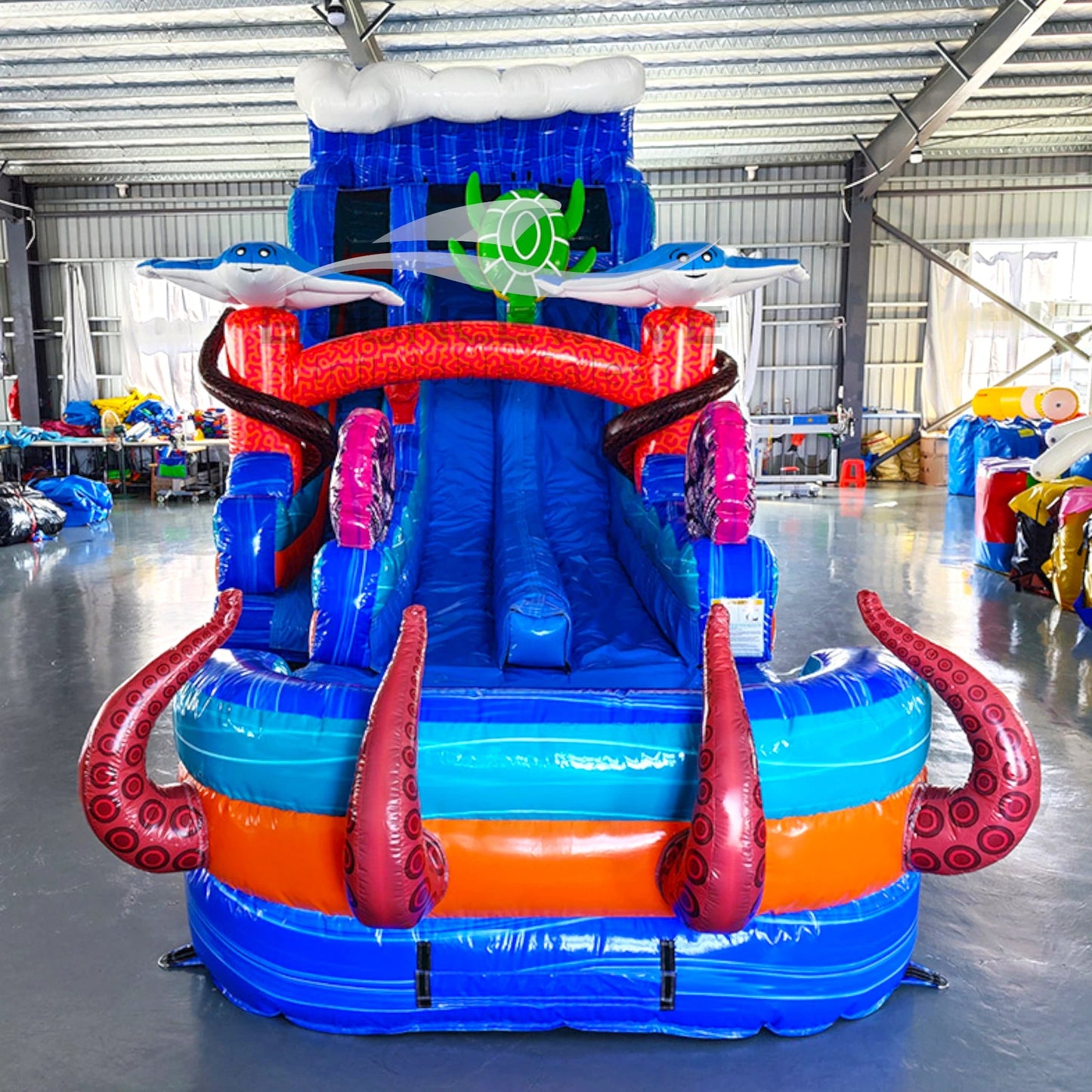 Front view of 20ft Reef Racer Hybrid DL water slide showing bright blue design, inflatable shark and stingray figures, and a large splash pool area with octopus tentacles. The slide features both open and enclosed sliding sections, displayed in an indoor facility.