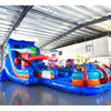 Side angle view of the 20ft Reef Racer Hybrid DL inflatable water slide, showcasing its blue sliding lanes, shark and stingray decorations, and spacious splash pool with octopus tentacles. The slide is set up in an indoor warehouse with other inflatables visible in the background.