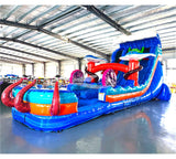Large inflatable water slide with ocean theme, featuring vibrant blue colors, shark and stingray decorations, and a spacious splash pool area with octopus tentacles. The slide combines open and enclosed sections, set up in an indoor warehouse with metal roofing visible.