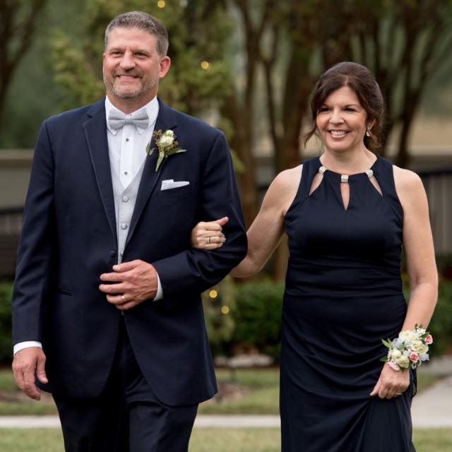 Chris Dious, Warehouse & Shipping Director, posing with a woman in formal attire at an outdoor event, surrounded by trees and a gravel path