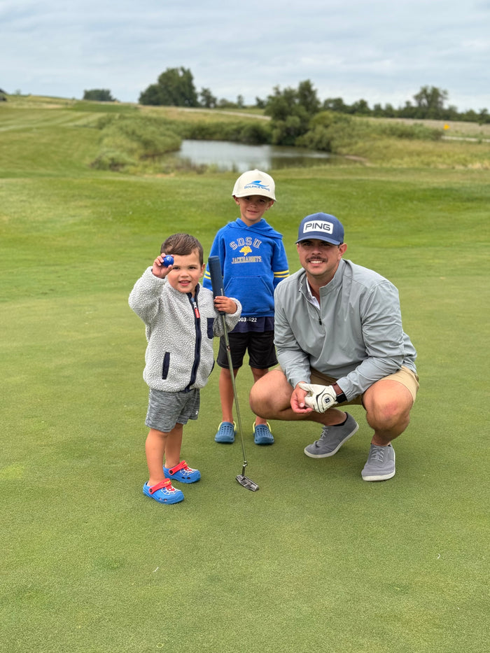 Austin Ladd, Product Design & Marketing Director, golfing with two young boys on a green course, showcasing family-friendly outdoor activities