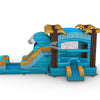 Side view of Akua Falls Commercial Econo Inflatable Combo (Wet/Dry) set up in an indoor warehouse. Features a blue wave-shaped structure with white foam crest, brown palm tree pillars, and yellow leaves. Shows the curved slide, bounce house area with mesh windows, and splash pool. Metal roofing and other warehouse equipment visible in the background.