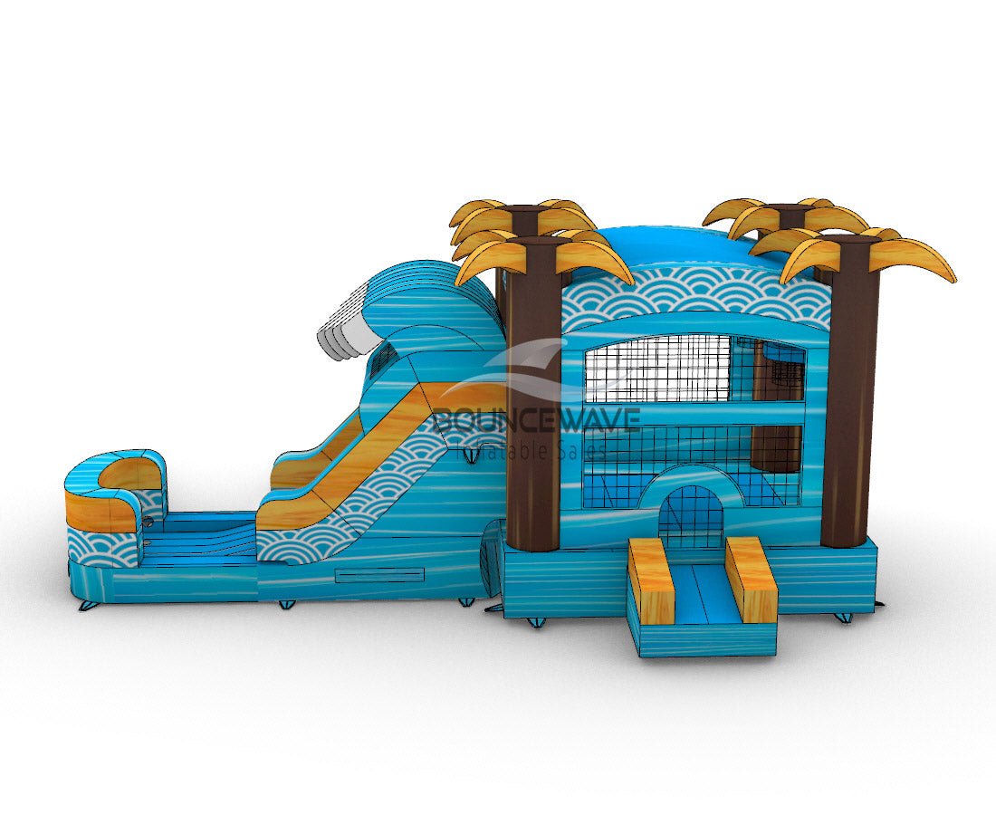 Side view of Akua Falls Commercial Econo Inflatable Combo (Wet/Dry) set up in an indoor warehouse. Features a blue wave-shaped structure with white foam crest, brown palm tree pillars, and yellow leaves. Shows the curved slide, bounce house area with mesh windows, and splash pool. Metal roofing and other warehouse equipment visible in the background.