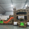Angled view of the Camo Econo Combo featuring a camouflage-patterned bounce house with turrets, orange slide, and green splash pool. The inflatable is set up in an indoor warehouse with metal roofing and other equipment visible in the background.