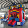 Front view of Carnival Econo Combo, showcasing the bounce house entrance with red pillars, blue and yellow spires, and a colorful awning. The combo includes a slide and splash pool area. Displayed in an indoor facility with metal roofing and other equipment visible.