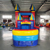 Side view of Carnival Econo Combo showing bright red, blue, and yellow design with multiple spired turrets. The combo includes a bounce house, slide, and colorful splash pool area. Set up in an indoor warehouse with other inflatable products and equipment visible.