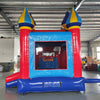 Large inflatable carnival-themed combo featuring a bounce house with colorful spires, attached slide, and splash pool. The structure has vibrant red, blue, and yellow colors with multiple castle-like turrets. Set up in an indoor warehouse with metal roofing and other inflatable products visible in the background.