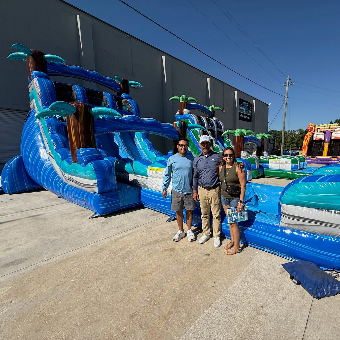 Three people standing in front of a large inflatable water slide and obstacle course.