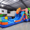 Wide-angle view of Deep Sea Dive Dual Lane Commercial Inflatable Combo in a spacious warehouse. The inflatable features dual blue slides, a large orange octopus, green tentacles, and a blue wave-patterned base with a splash pool. Metal roofing, support beams, and other inflatable products visible in the background, demonstrating its size and commercial setting.