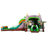 Large dinosaur-themed inflatable combo featuring a gray castle structure with green accents and flame-topped towers. Two realistic T-Rex figures flank the entrance. The combo includes dual slides, a bounce area, and inflatable foliage. Set against a white background, showcasing its prehistoric design for commercial wet/dry use.