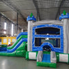 Wide-angle view of Euro Green Gush Commercial Econo Inflatable Wet/Dry Combo featuring a blue and silver castle-themed bounce house with green turrets, slide, and splash pool area. The inflatable is set up in a large indoor warehouse with metal roofing, bright lighting, and other inflatable products visible.