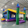 Front view of Goombay Commercial Grade Canopy Bounce House featuring a vibrant blue inflatable structure with four tall pillars topped by white cylindrical turrets and blue conical roofs. The bounce area has yellow walls with mesh windows. A yellow canopy extends between the turrets, creating a covered play space. Set up in a large indoor warehouse with metal roofing and other inflatable products visible in the background.