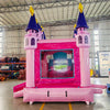 Close-up Rear view of Grand Royal Castle Commercial Econo Inflatable Combo (Wet/Dry) entrance. Shows detailed pink castle facade with purple turrets, yellow flags, and mesh-covered openings. Set up in a warehouse with other inflatable products and equipment visible in the background, emphasizing its design and commercial use.