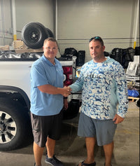 Flower Town Party Rentals testimonial: Bryce H. shaking hands with a Bouncewave representative in front of a large black trailer, showcasing successful business partnership