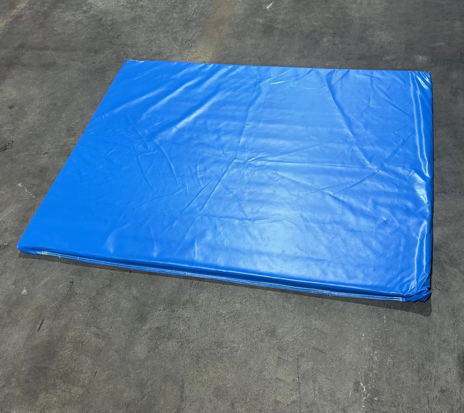 Impact Safety Mat for Inflatables displaying large blue padded surface with sewn edges on concrete floor
