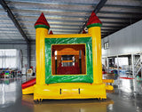 Front view of Rasta Splash Commercial Econo Inflatable Combo (Wet/Dry) set up in an indoor warehouse. Features yellow walls, red turrets, green frame, and a mesh-covered entrance. The inflatable includes a curved slide and splash pool area. Metal roofing and other warehouse equipment visible in the background.