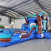Large inflatable tropical-themed combo featuring a bounce house with palm tree decorations, attached slide, and splash pool. The structure has vibrant blue and turquoise colors with brown palm tree trunks and a large inflatable sunglasses decoration on top. Set up in an indoor warehouse with metal roofing and other inflatable products visible in the background.